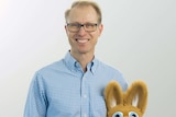 A blond man with glasses holding a kangaroo puppet