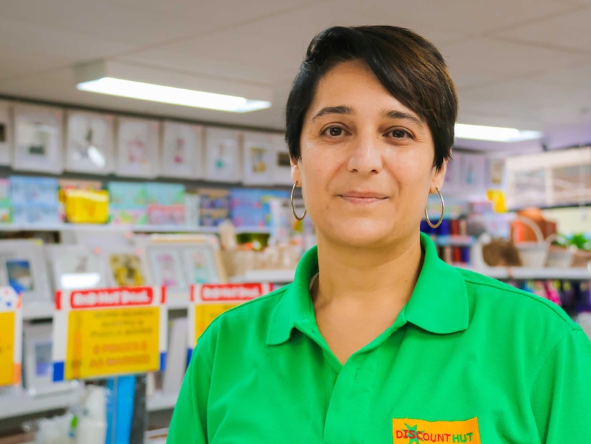 A woman with short brown hair in a bright green shirt standing in a discount store.