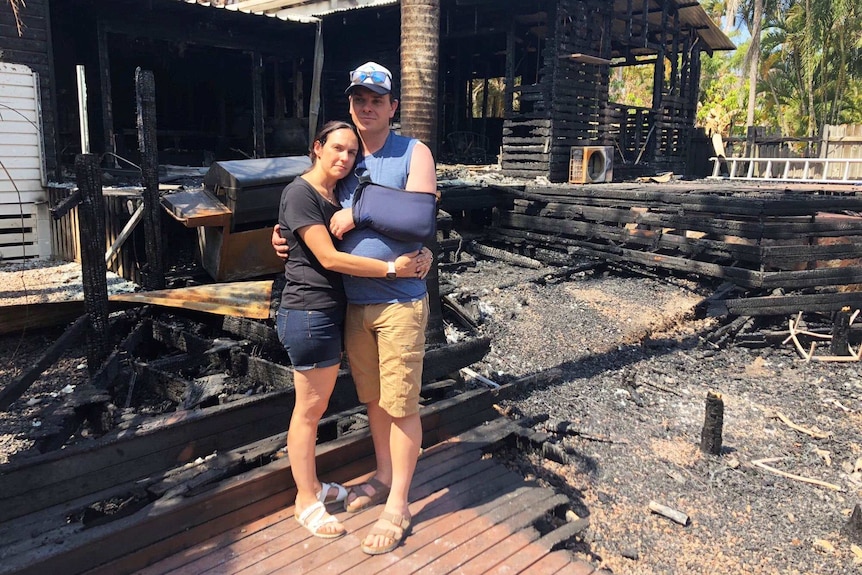Holly and David Kemp hug as they stand in the bushfire-destroyed remains of their home at Lake Cooroibah Road.