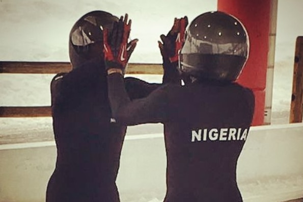Two women in black bobsled outfits 'high 10' each other.