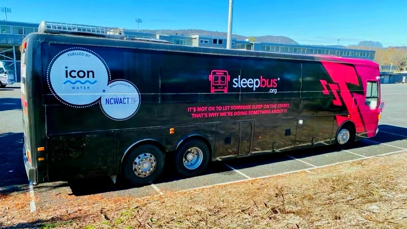 A black and pink large bus sits in a car park in Canberra