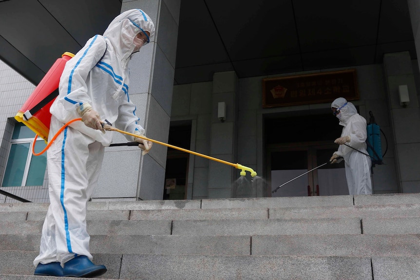 Two people in full PPE spraying disinfectant on a staircase 
