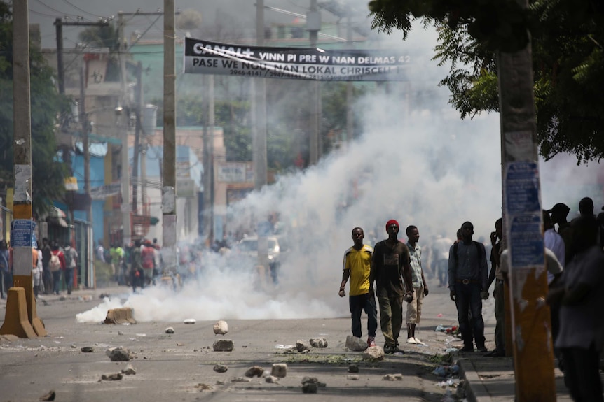 Men stand in a street shrouded in tear gas during a protest.