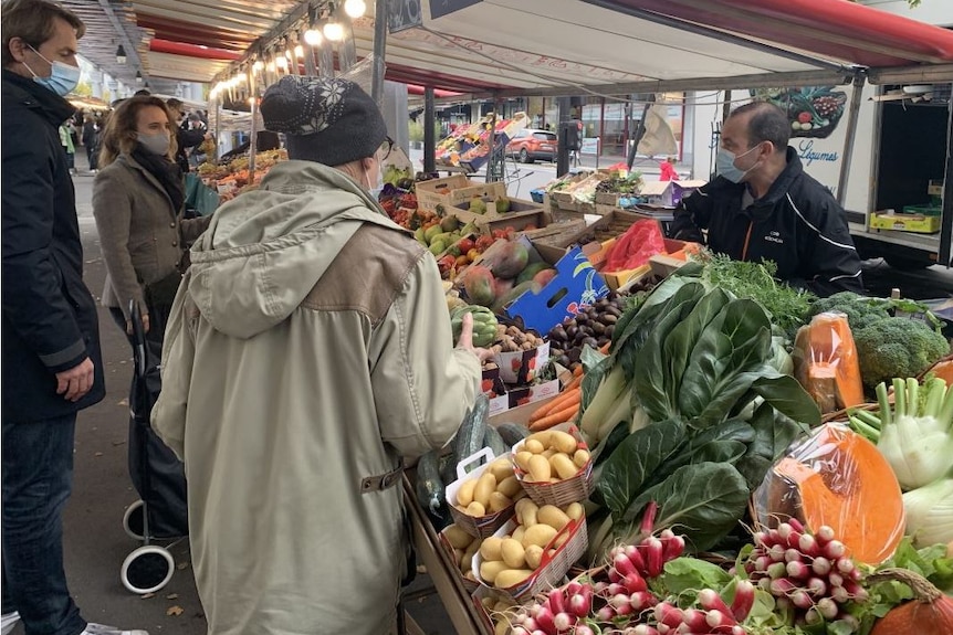 People wearing masks shop at an outdoor market.