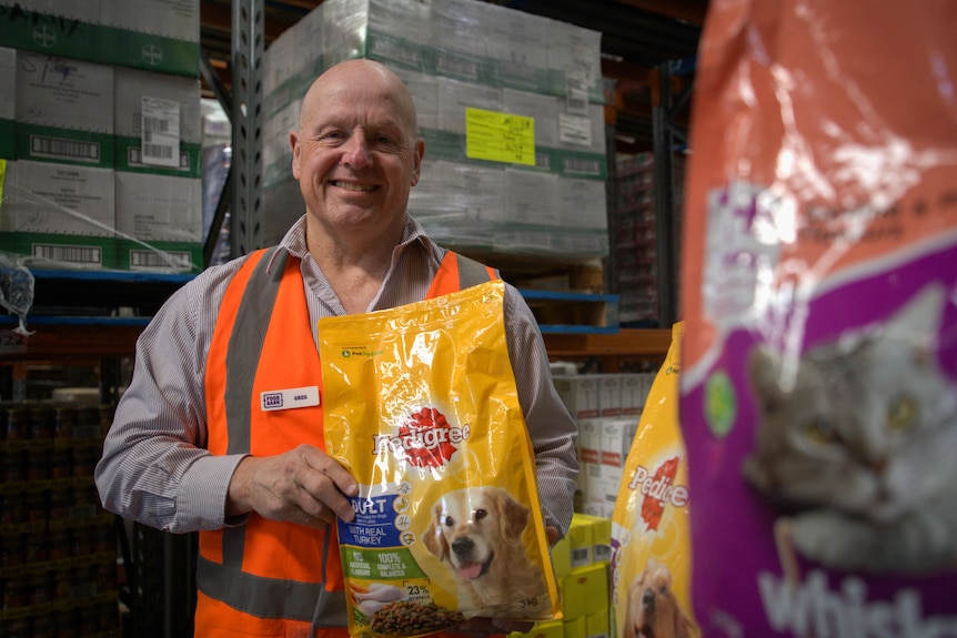 A man with a high vis vest smiles as he holds a big bag of dog food