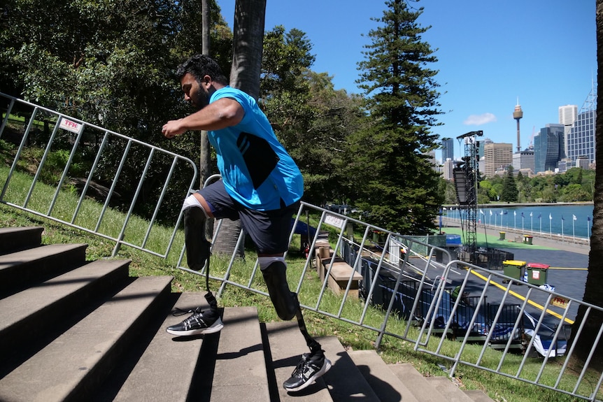 A man with two prosthetic legs runs up stairs outside with a city skyline in the background