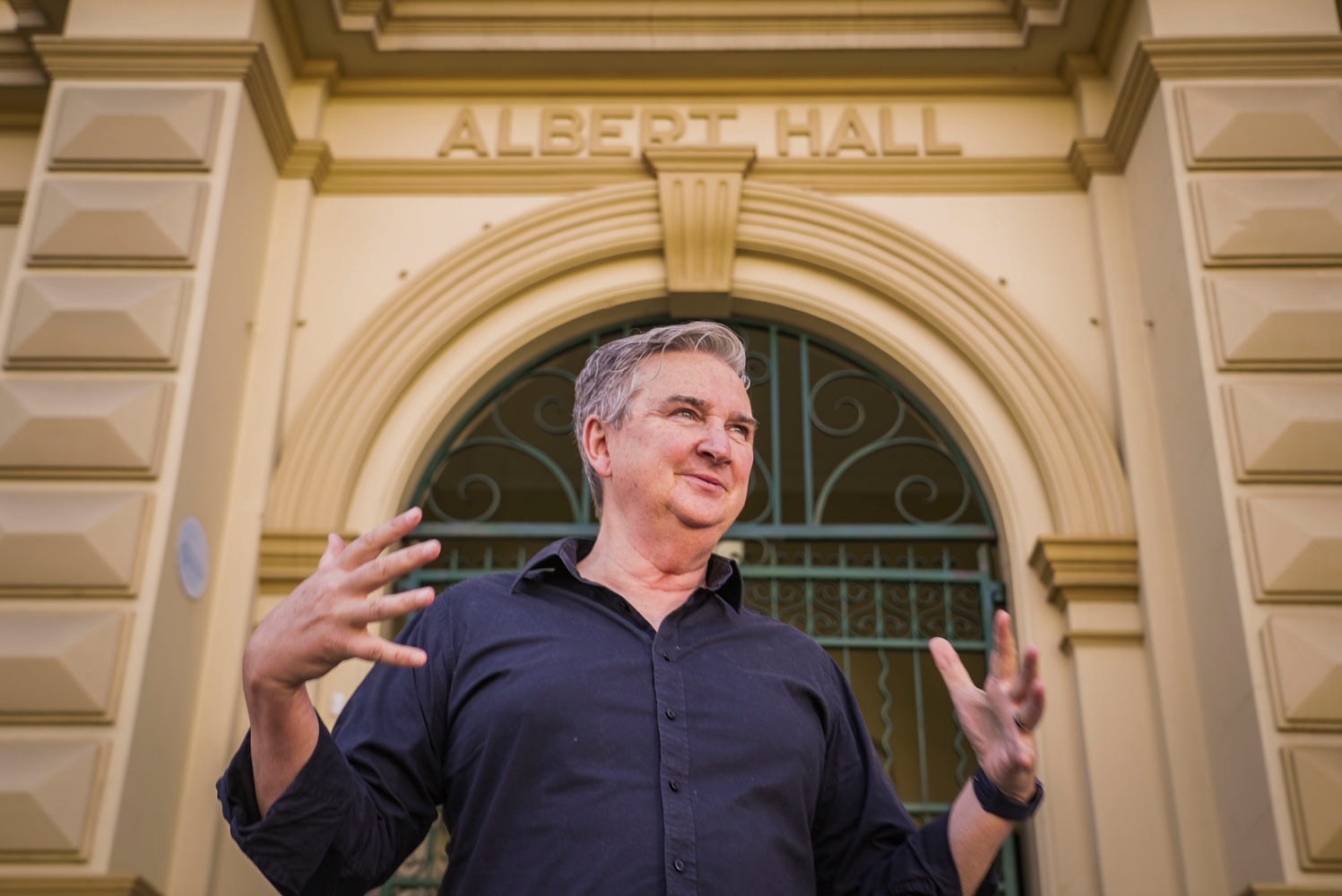 a man with a navy shirt and grey hair out the front of a yellow building