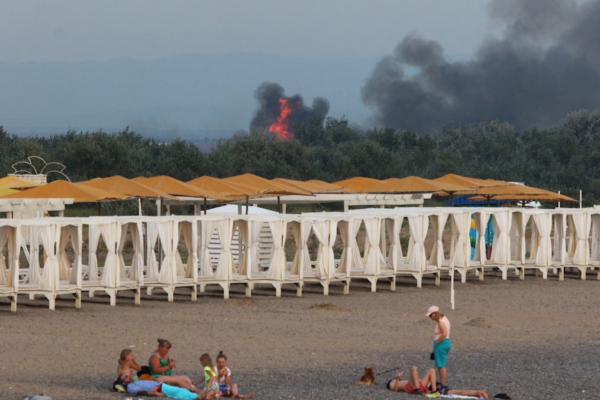 people sitting on beach with smoke in the background. 