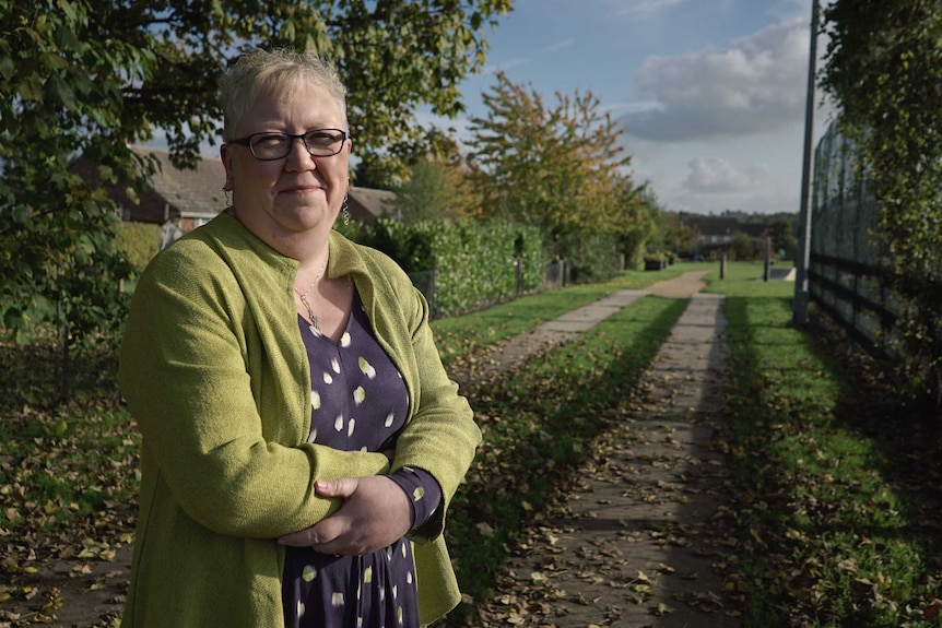 Carla Hales stands near a field while holding her arms crossed.