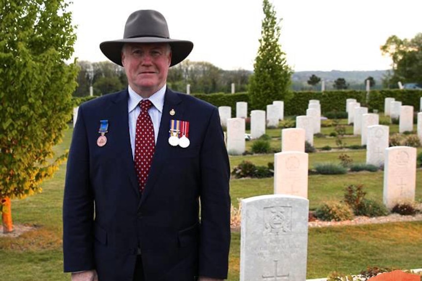 A man wearing a broad-brimmed hat and a blazer with medals, standing in graveyard.