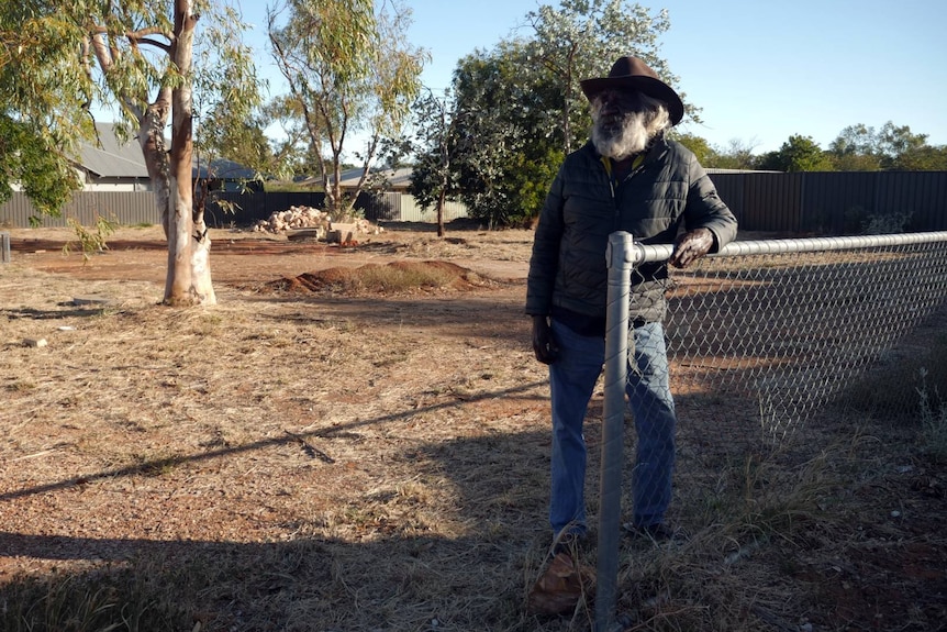 An Indigenous man leans against a fence.