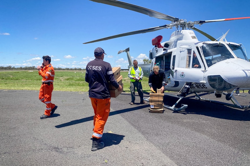 A man carrying boxes to load into a helicopter with other men helping