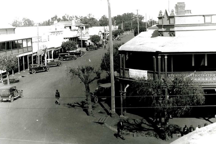 A black and white photo from the 1920s, showing streets and cars and shop front in a rural town.