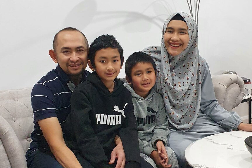 A family of four looking at the camera and smiling. The mother is wearing hijab.