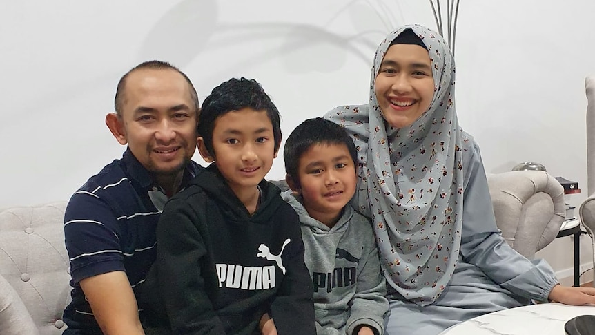 A family of four looking at the camera and smiling. The mother is wearing hijab.