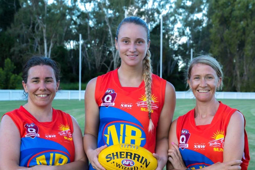 Three women in AFL jerseys stand holding a ball