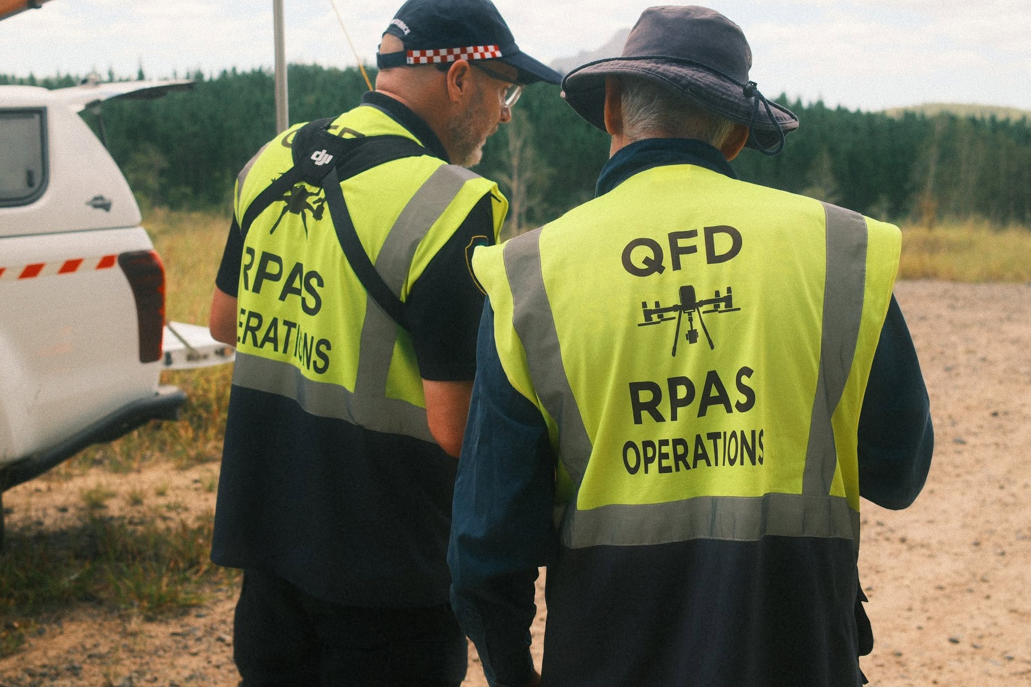 Two QFD personnel standing, wearing vests with drone symbols.