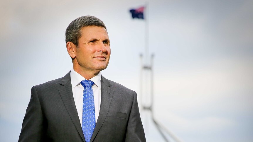 Chris Uhlmann stands in front of Parliament House, looking into the distance with a furrowed brow.