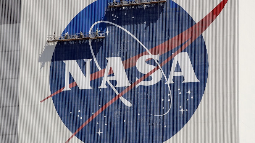 Workers on scaffolding repaint the NASA logo near the top of the Vehicle Assembly Building at the Kennedy Space Center