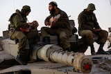 Israeli soldiers play guitars while sitting on top of a tank.