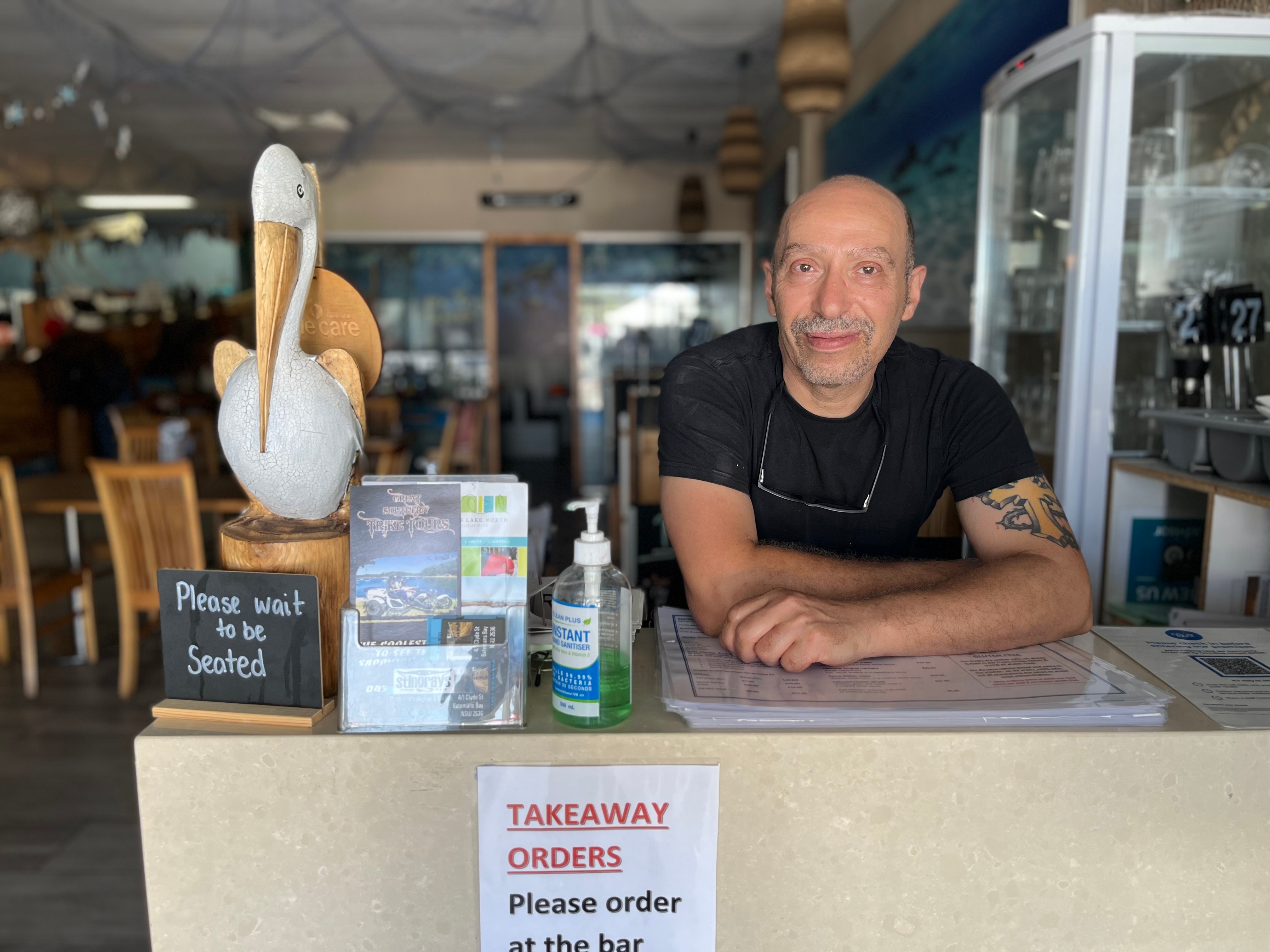 A man leans on a desk looking at the camera. 