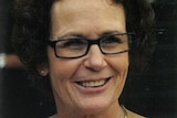 A woman with curly brown hair and black glasses