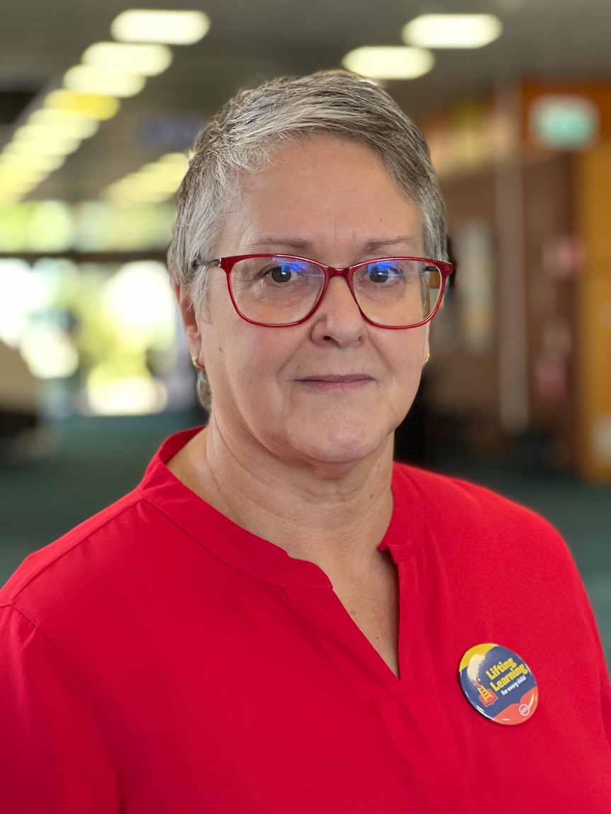 A woman with a red top and red glasses looks at the camera.