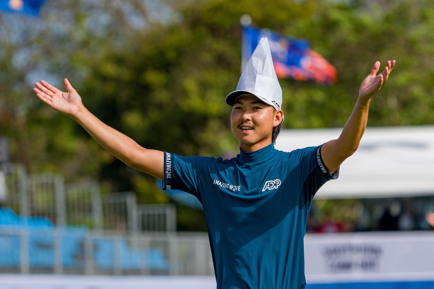 Golfer wearing blue polo throws hands in the air while wearing a white chef's hat. He is smiling