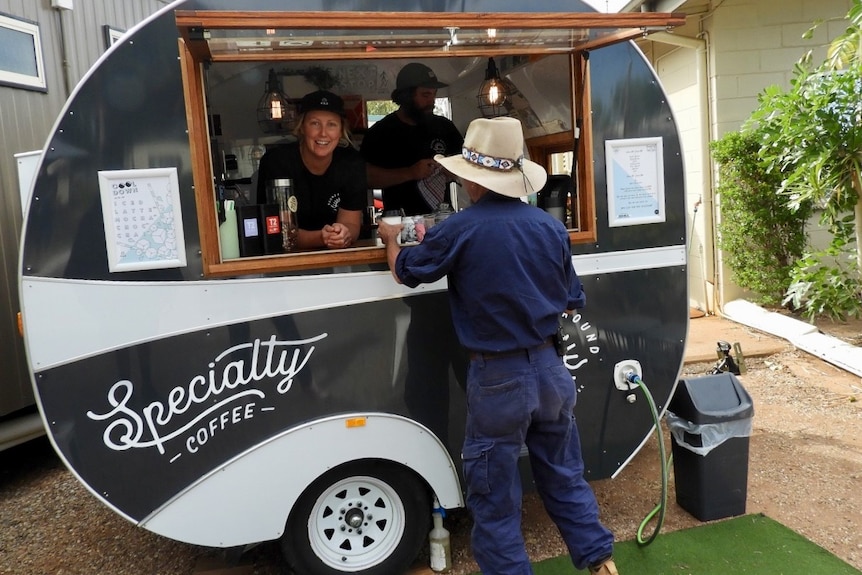 Man with big hat stands at window of coffee caravan