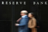 Two blurred people walking past a black wall with 'Reserve Bank' in white lettering.