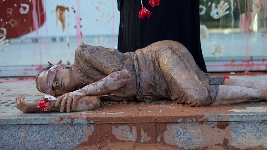 A woman covered in mud with a sash over her eyes lies in front of the granite steps of Vale SA's headquarters.