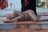 A woman covered in mud with a sash over her eyes lies in front of the granite steps of Vale SA's headquarters.
