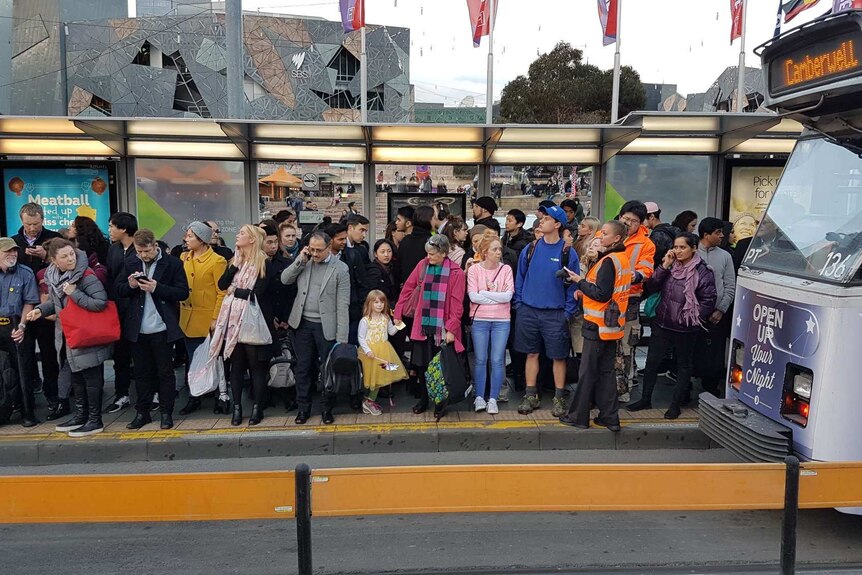 People on a crowded tram stop outside Flinders Street Station.