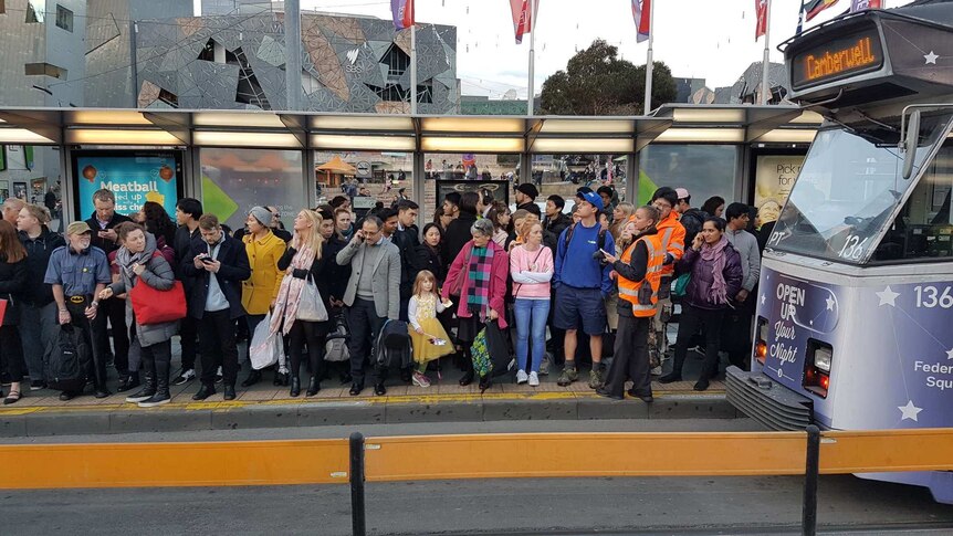 People on a crowded tram stop outside Flinders Street Station.
