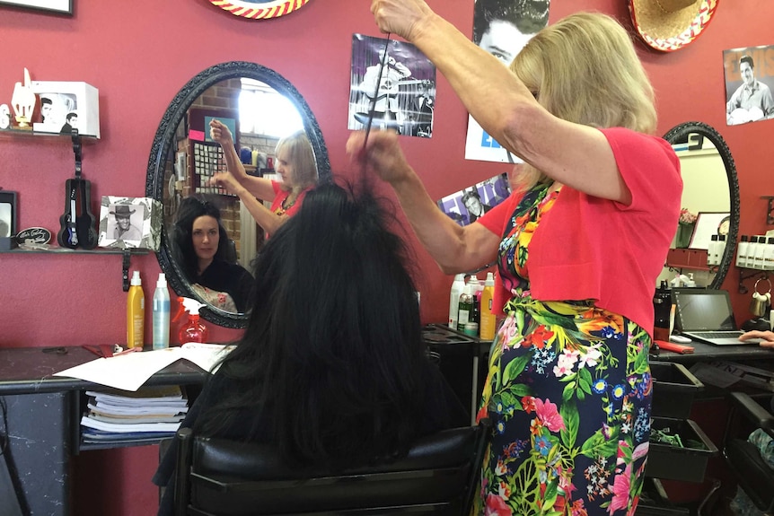A hairdresser styles a woman's long hair in front of a mirror