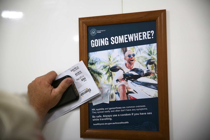 A man leans on a wall, with an HIV awareness poster in front of a urinal