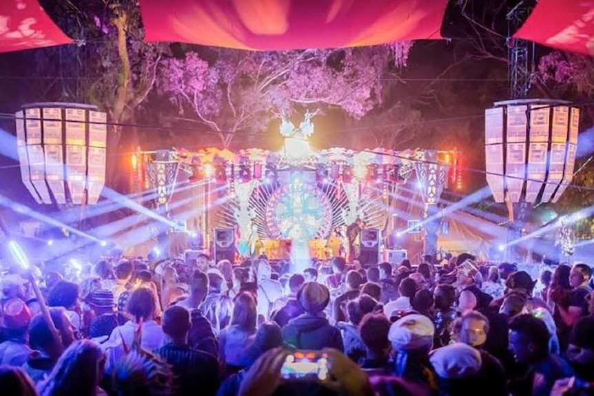 A crowd of people stand in front of a stage lit with lasers and bright, colourful lights