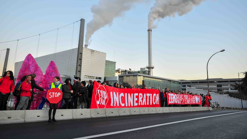 Protestors in front of a plant with smoke emissions
