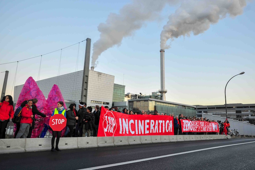 Protestors in front of a plant with smoke emissions