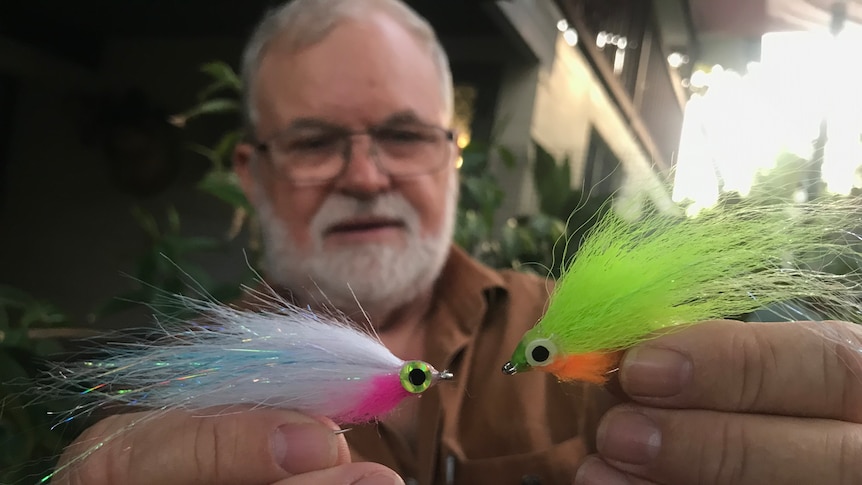 Roger Sinclair holding two barra fishing flies in Darwin