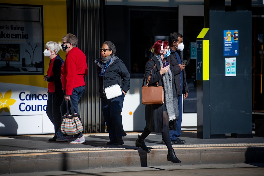 People wearing face masks at a tram stop with a tram behind