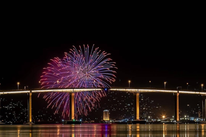 A bridge with 2 purple and pink fireworks over it