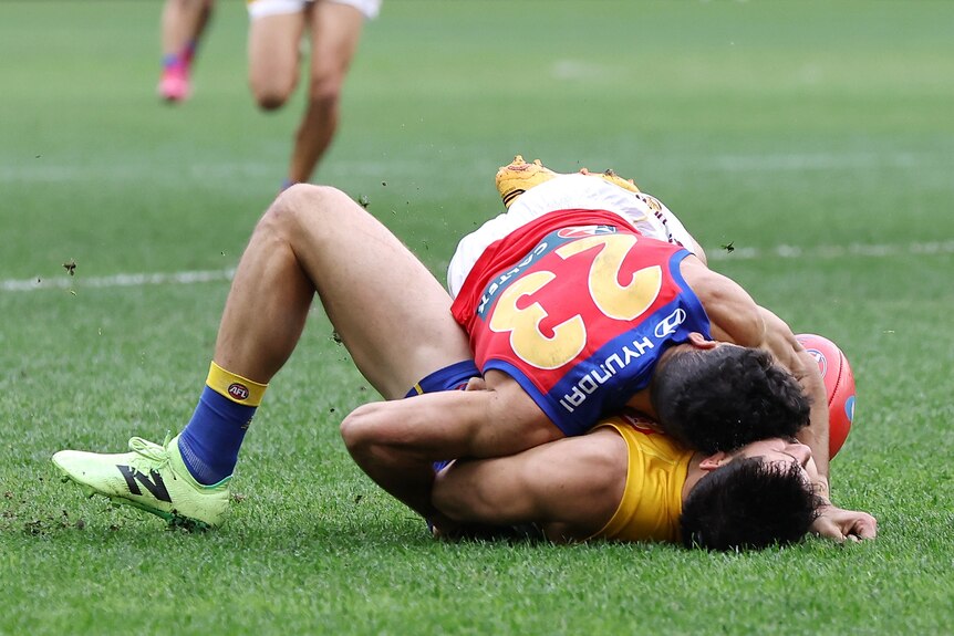 A West Coast AFL player lies on the ground after being tackled as a Brisbane forward lies on top of him. 