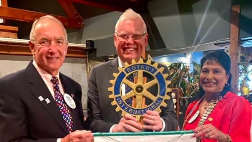 Two men and a woman stand smiling at a camera holding some Rotary signs