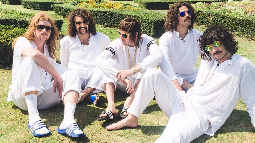 Sticky Fingers in cricket whites sitting on hedge maze lawn