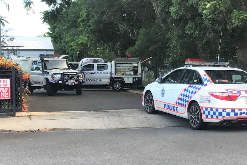 Three police cars parked behind a minibus at a school gate