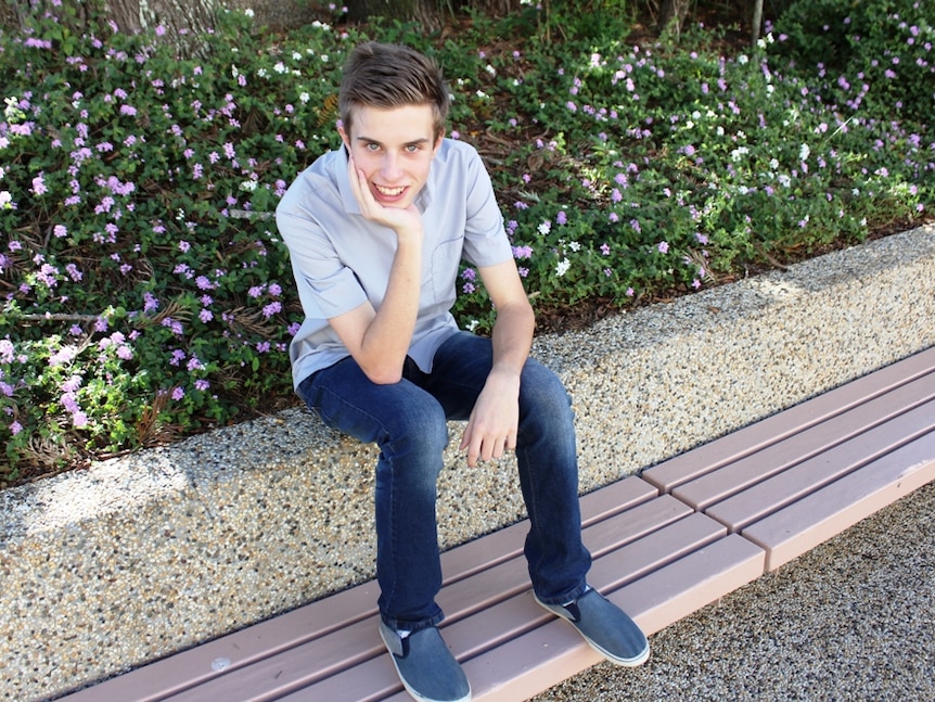 15 year old student Samuel Bouzanquet sits on a sit with bushes behind, head leaning on his hand