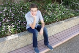 15 year old student Samuel Bouzanquet sits on a sit with bushes behind, head leaning on his hand