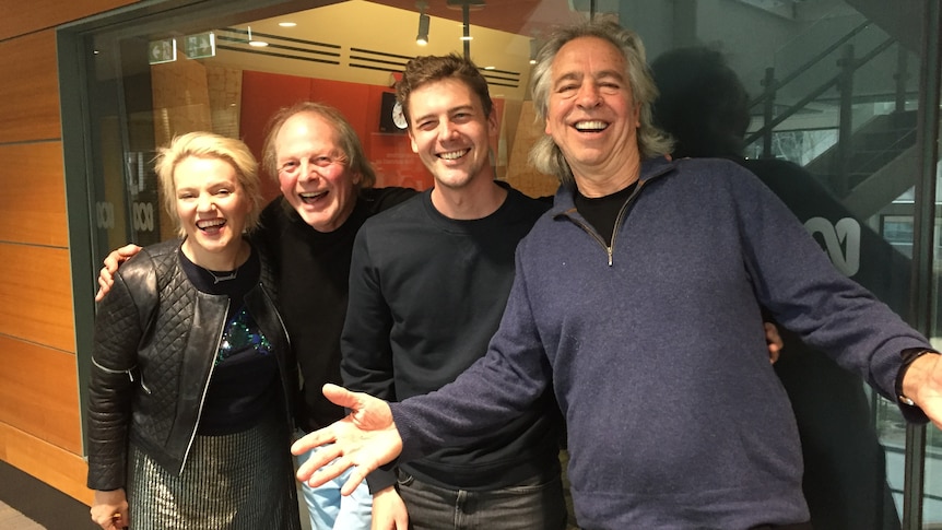 one woman and three men smiling outside a radio studio with glass walls