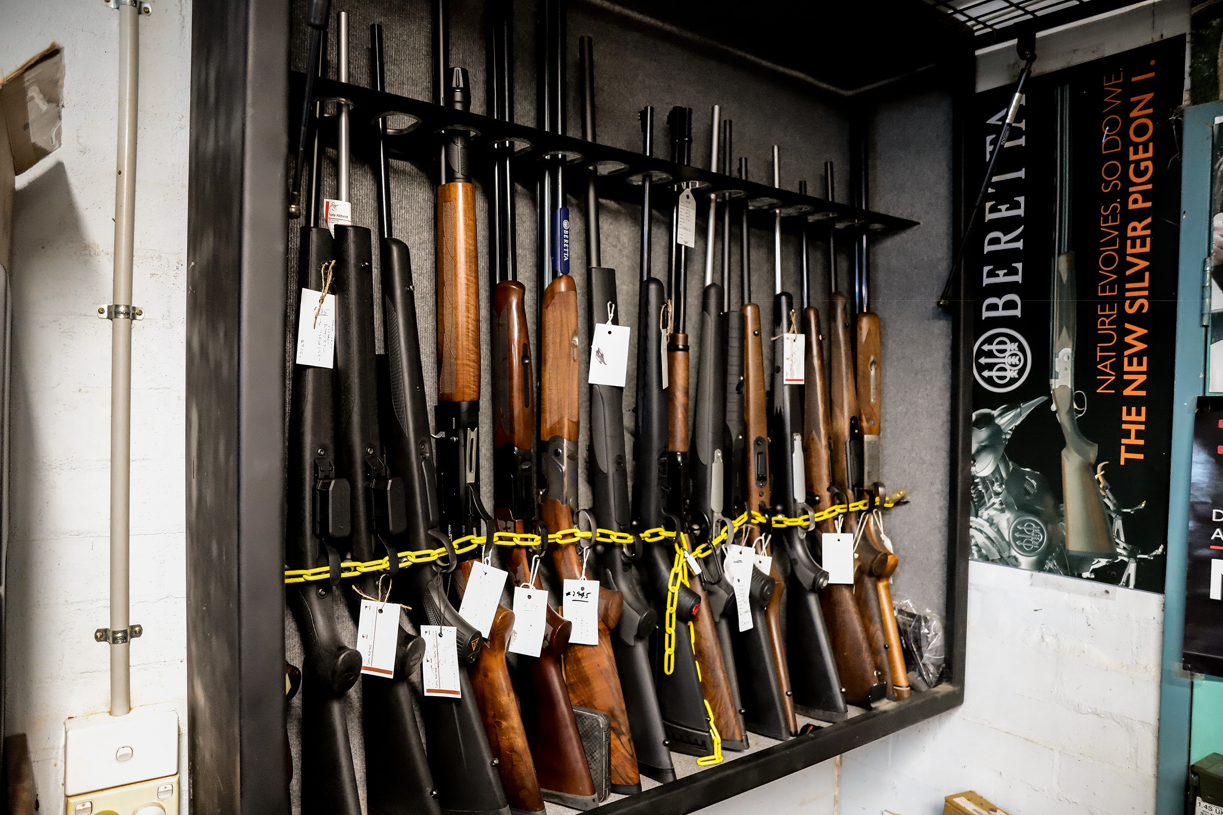An open cabinet with a rack of rifles sitting with their barrel facing up. There is a bar locking them in at the top and a chain
